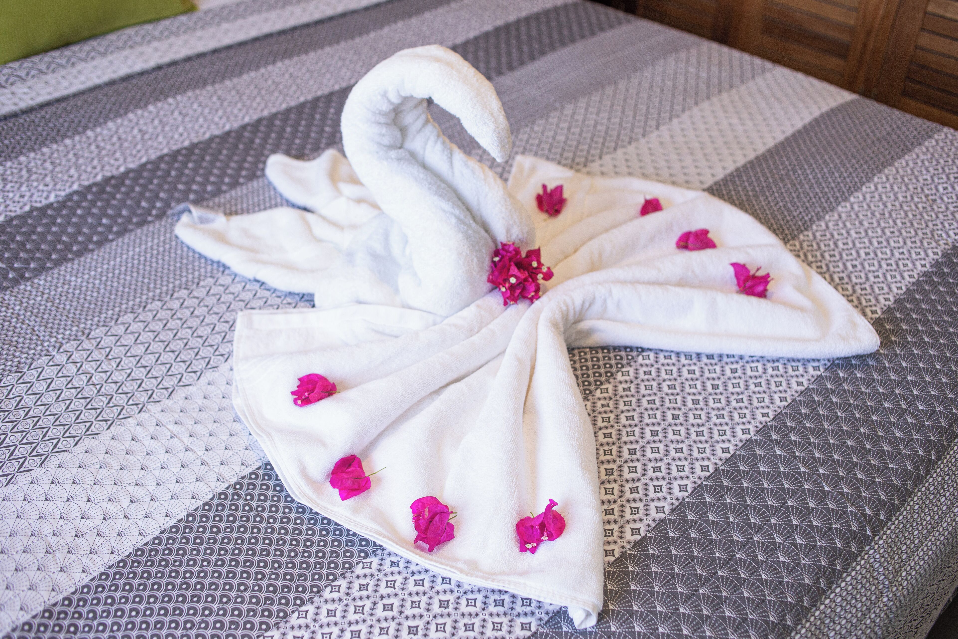 A bed with a white towel arranged in a swan shape, adorned with pink flowers.