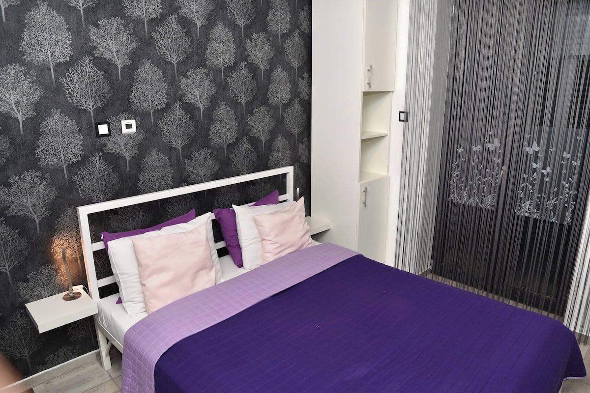 A bedroom with a bed, nightstands, a dresser, and a window with curtains.