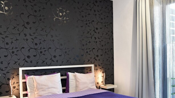 Un dormitorio moderno con una cama grande, un papel tapiz estampado y vistas al exterior a través de una ventana con cortinas.