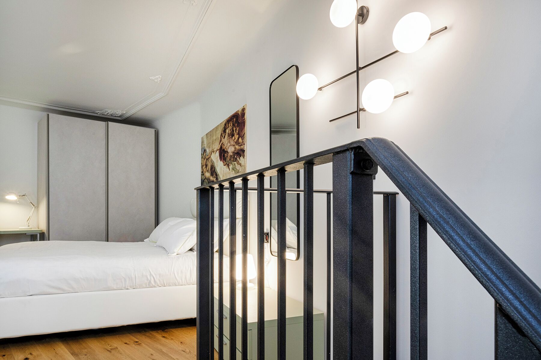 Une chambre à coucher comprenant un lit, une table de chevet, une lampe de bureau, un tableau et un escalier avec une rampe.