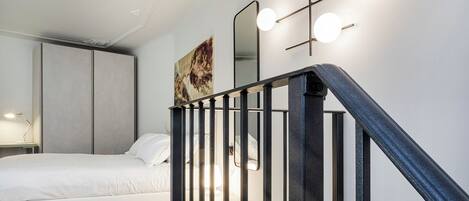 Une chambre à coucher comprenant un lit, une table de chevet, une lampe de bureau, un tableau et un escalier avec une rampe.