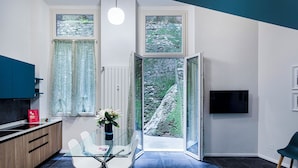 Ett modernt kök med ett matbord i glas, vita stolar och utsikt över ett bergigt landskap genom stora fönster.