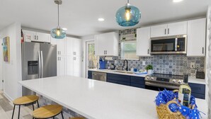 A modern kitchen with white cabinets, stainless steel appliances, a large island with stools, and decorative blue and white tiles. - Private Coastal home w. gaming loft, pool table, hot tub, arcades - pet friendly (Hudson)
