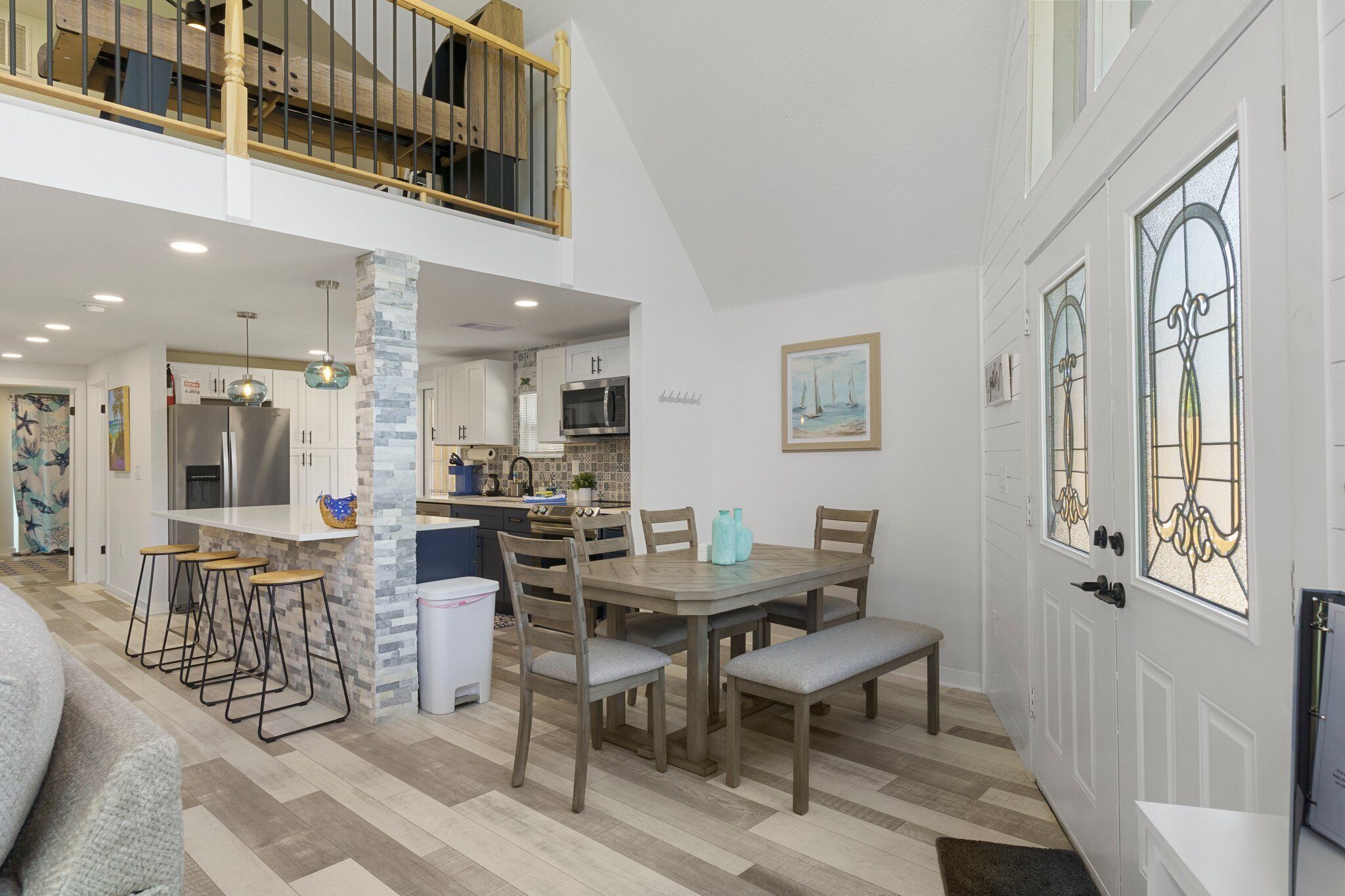 Une cuisine spacieuse avec un coin repas, un escalier menant à l’étage supérieur et une porte décorative ornée de vitraux.