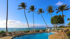A poolside area with lounge chairs, palm trees, and a view of the ocean. - Discover Paradise at Royal Mauian | Ground Floor Oceanview and Island Living (Kihei)