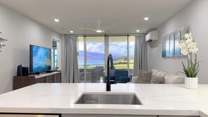 A modern kitchen with a large island, a built-in dishwasher, and a view of the outdoors. - Discover Paradise at Royal Mauian | Ground Floor Oceanview and Island Living (Kihei)