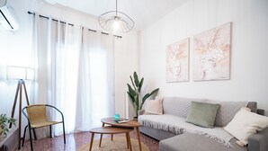 Ein modernes Wohnzimmer mit grauem Sofa, einem Korbstuhl, einem kleinen Holztisch und einer großen Pflanze.