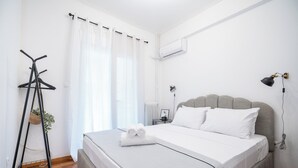 Ein ordentlich bezogenes Bett mit weißen Leinentextilien, einem grau gepolsterten Kopfteil und einem Nachttisch mit einer Lampe.