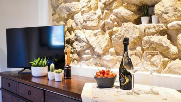 A stone wall, a flat-screen TV, a wine bottle, and a bowl of fruit on a wooden table. - Il Vicoletto Marostica - ITALY (Marostica)