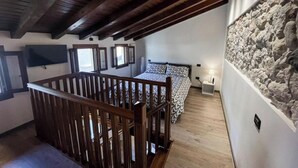 A bedroom with a wooden ceiling, a stone wall, a bed with patterned bedding, and a nightstand with a lamp. - Il Vicoletto Marostica - ITALY (Marostica)