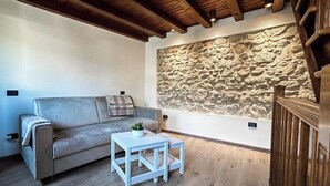 A cozy living room with a stone wall, a grey sofa, a small white table, and a wooden ceiling. - Il Vicoletto Marostica - ITALY (Marostica)