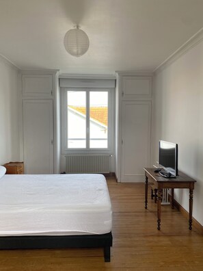 A bedroom with a bed, a television on a wooden table, and a window with a view of a building.