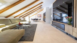 Un salon moderne avec un plafond haut, des poutres apparentes en bois, un canapé, une table basse et un coin cuisine avec une grande fenêtre.