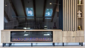 Un salon moderne doté d’un grand téléviseur à écran plat fixé au mur, d’une cheminée à vitrine et d’un meuble en bois avec des étagères.