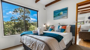A bedroom with a large window, a bed with multiple pillows, and a painting on the wall.