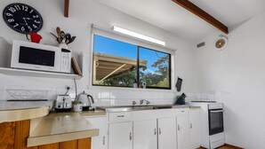 A kitchen with white cabinets, a microwave, a toaster, a sink, and a window with a view of trees.