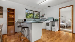 A compact kitchen with a central island, bar stools, a microwave, a stove, and a window overlooking greenery.