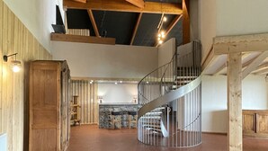 Un interior espacioso con techo alto, vigas de madera a la vista, una escalera central y una pared de acento en piedra.