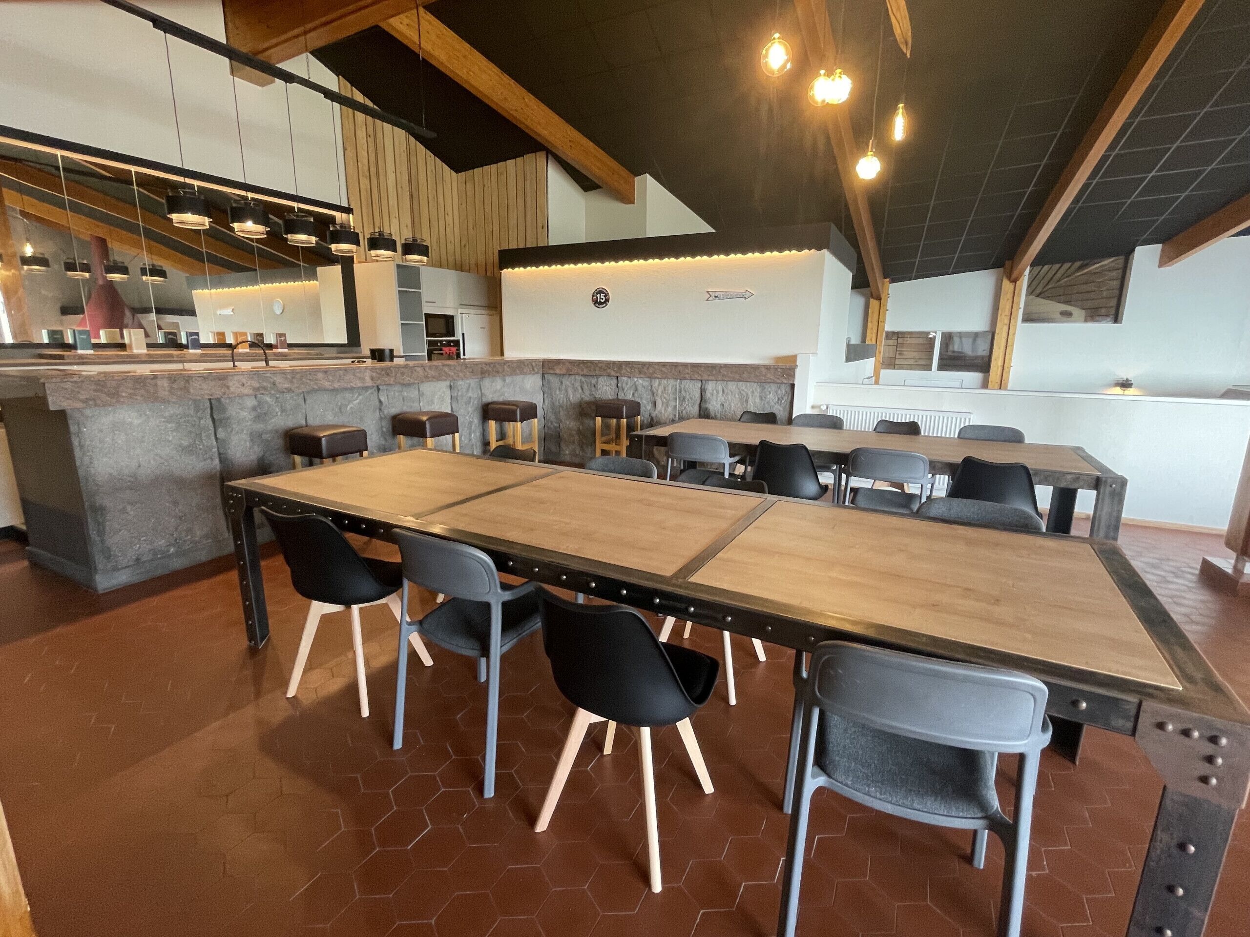 Un restaurant moderne doté d’une grande table conviviale, de plusieurs tabourets de bar et d’un espace cuisine situé à l’arrière-plan.