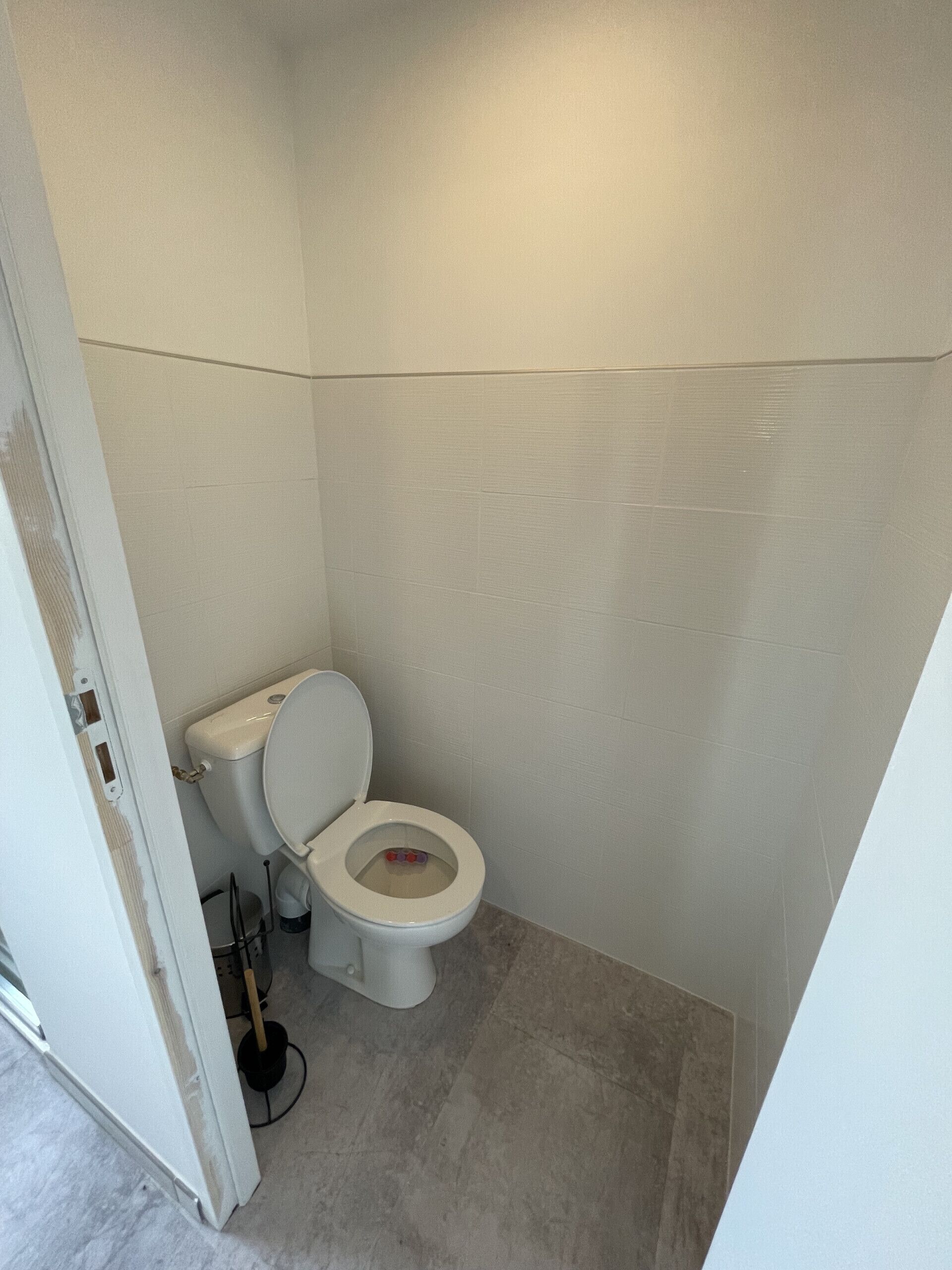 A small, white bathroom with a toilet, a visible plumbing pipe, and a tiled floor.