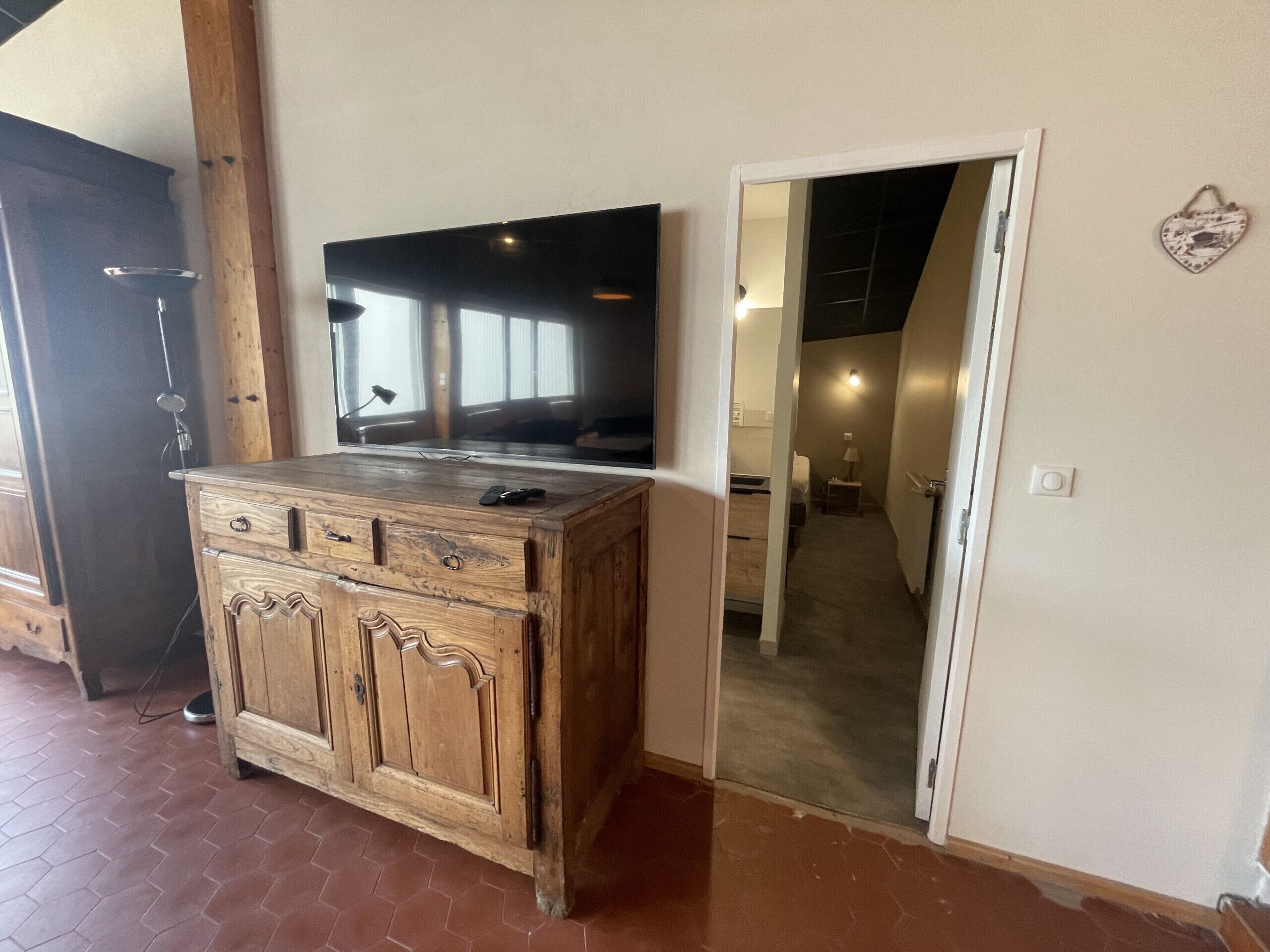 A wooden cabinet with drawers, a flat-screen TV mounted above it, and a door leading to a hallway.
