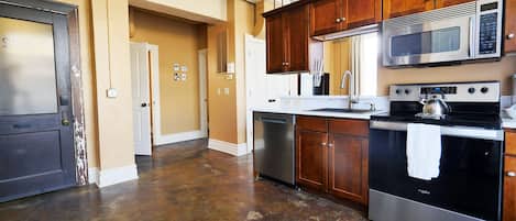 A kitchen with stainless steel appliances, wooden cabinets, and a tiled floor.