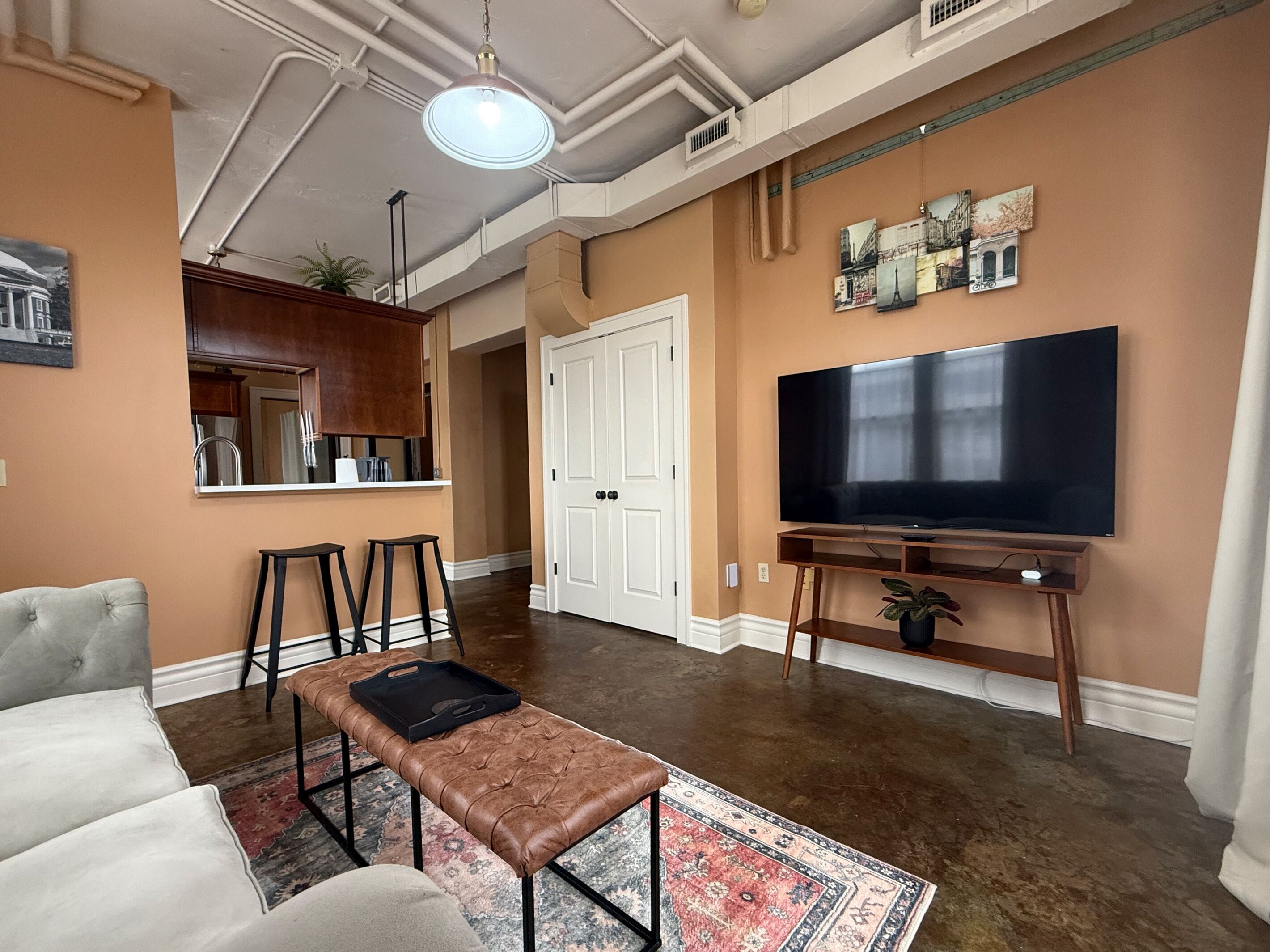 A living room with a sofa, a coffee table, a TV, and a kitchen area with cabinets and a countertop.