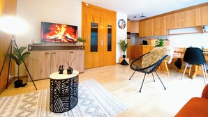 Un soggiorno moderno con TV a schermo piatto, un tavolino rotondo, una poltrona nera e un'area pranzo con mobili in legno.