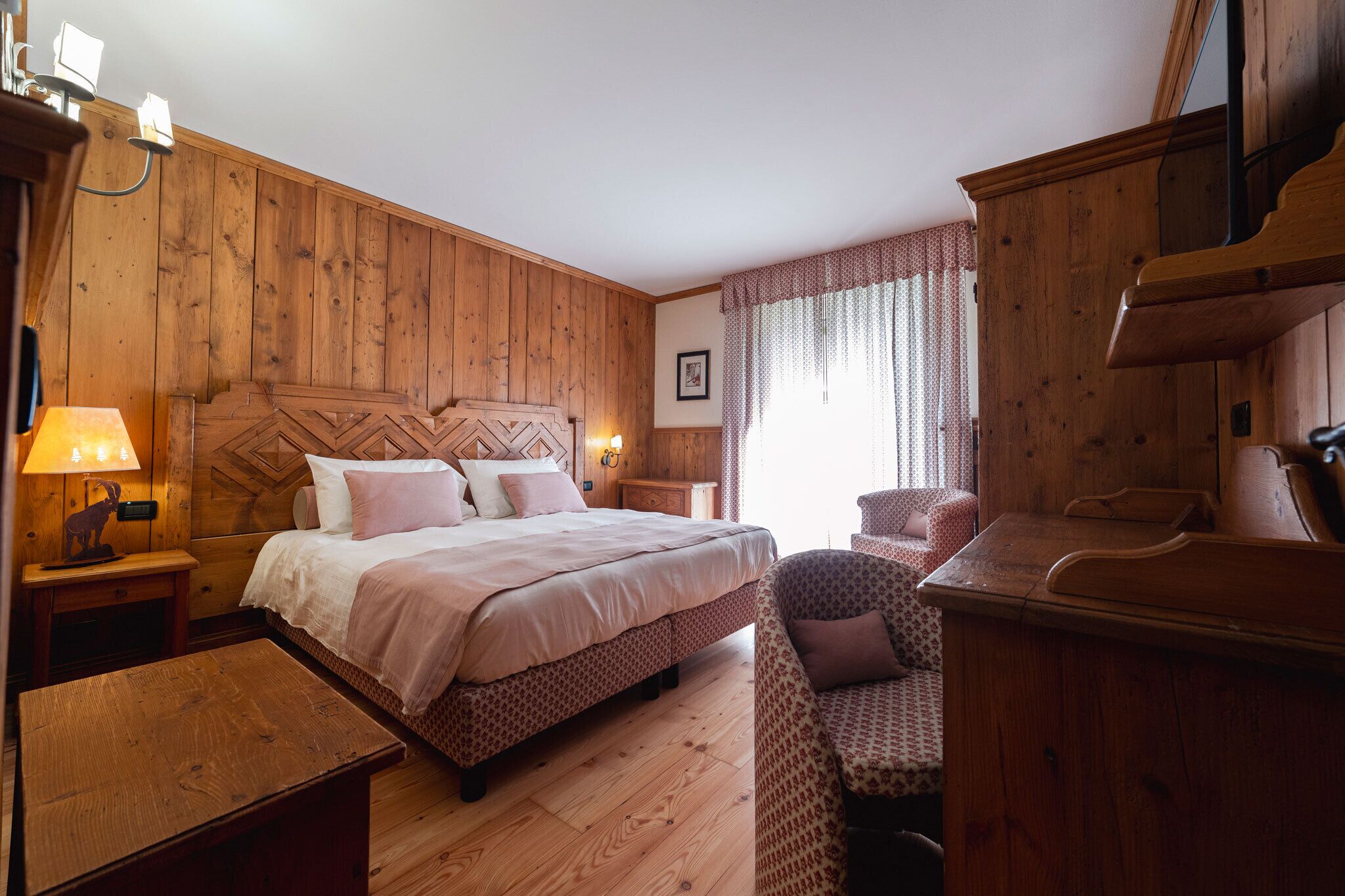 Ein schlafgemach im Holzstil mit einem Bett, Nachttischen, einem Sessel und einem Schreibtisch.