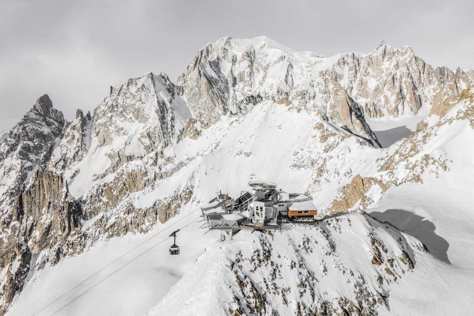 Un chalet de montagne avec un télésiège, entouré de sommets enneigés.