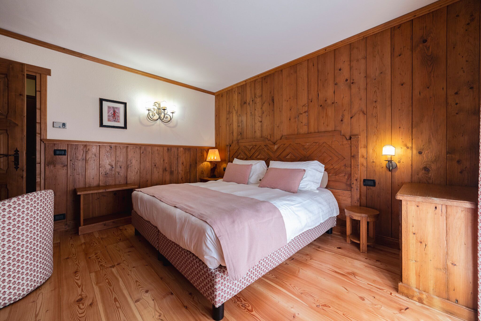 Ein Schlafzimmer mit Holzwandverkleidung, einem Bett, Nachttischlampen, einer Bank und einem kleinen Tisch.