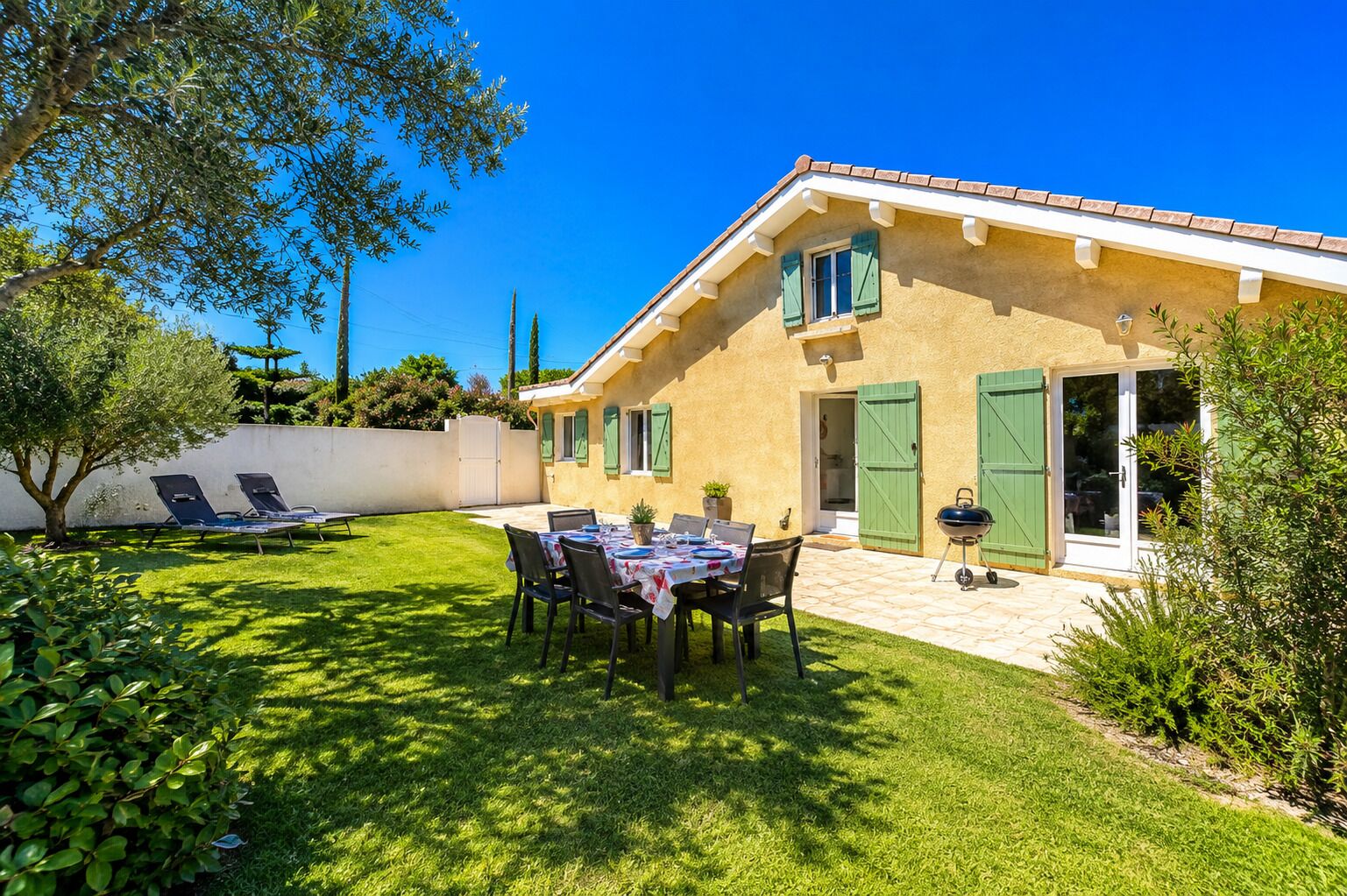 Ein Haus mit Terrasse, Tisch, Stühlen und Grill.