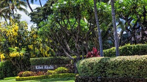 A well-maintained garden with a stone wall, lush greenery, and a sign reading "Kihei Akahi". - Oceanview Condo | Steps to Kamaole Beach II | Top-Floor Kihei Comfort w/ AC (Kihei)