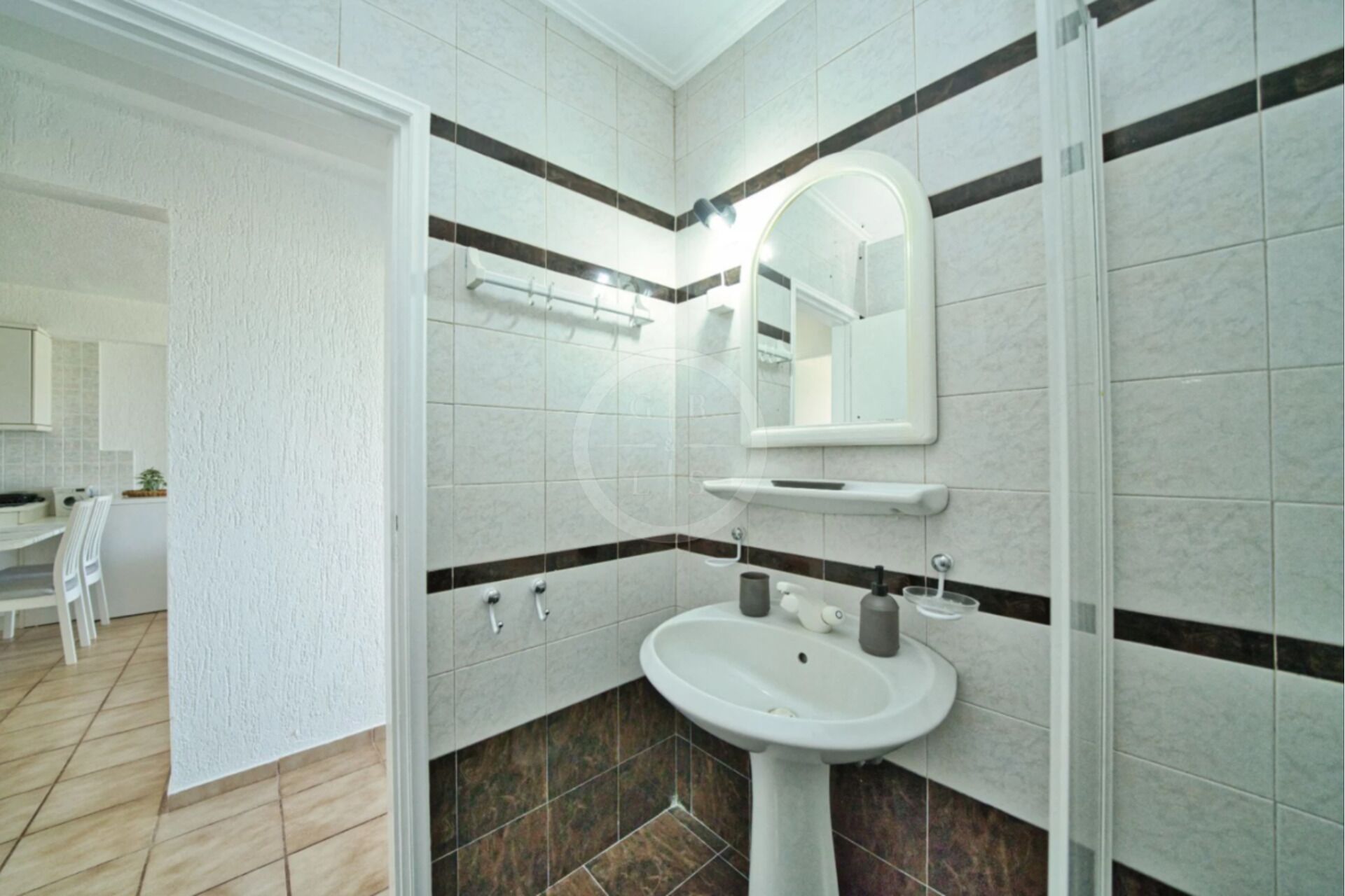 Un baño con lavamanos blanco, espejo y paredes con azulejos.