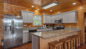 A kitchen with wooden walls, a stainless steel refrigerator, a microwave, and a granite countertop. - Papa Bear's Cabin – 8BR with stunning Mt. LeConte views (Gatlinburg)