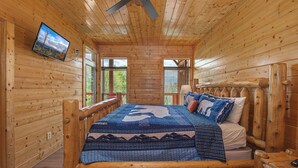 A wooden cabin bedroom with a bed, a television, and a ceiling fan. - Papa Bear's Cabin – 8BR with stunning Mt. LeConte views (Gatlinburg)
