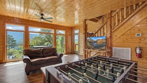 A wooden interior with a foosball table, a leather couch, and a television. - Papa Bear's Cabin – 8BR with stunning Mt. LeConte views (Gatlinburg)