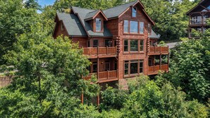 A large, multi-story wooden cabin surrounded by dense trees. - Papa Bear's Cabin – 8BR with stunning Mt. LeConte views (Gatlinburg)