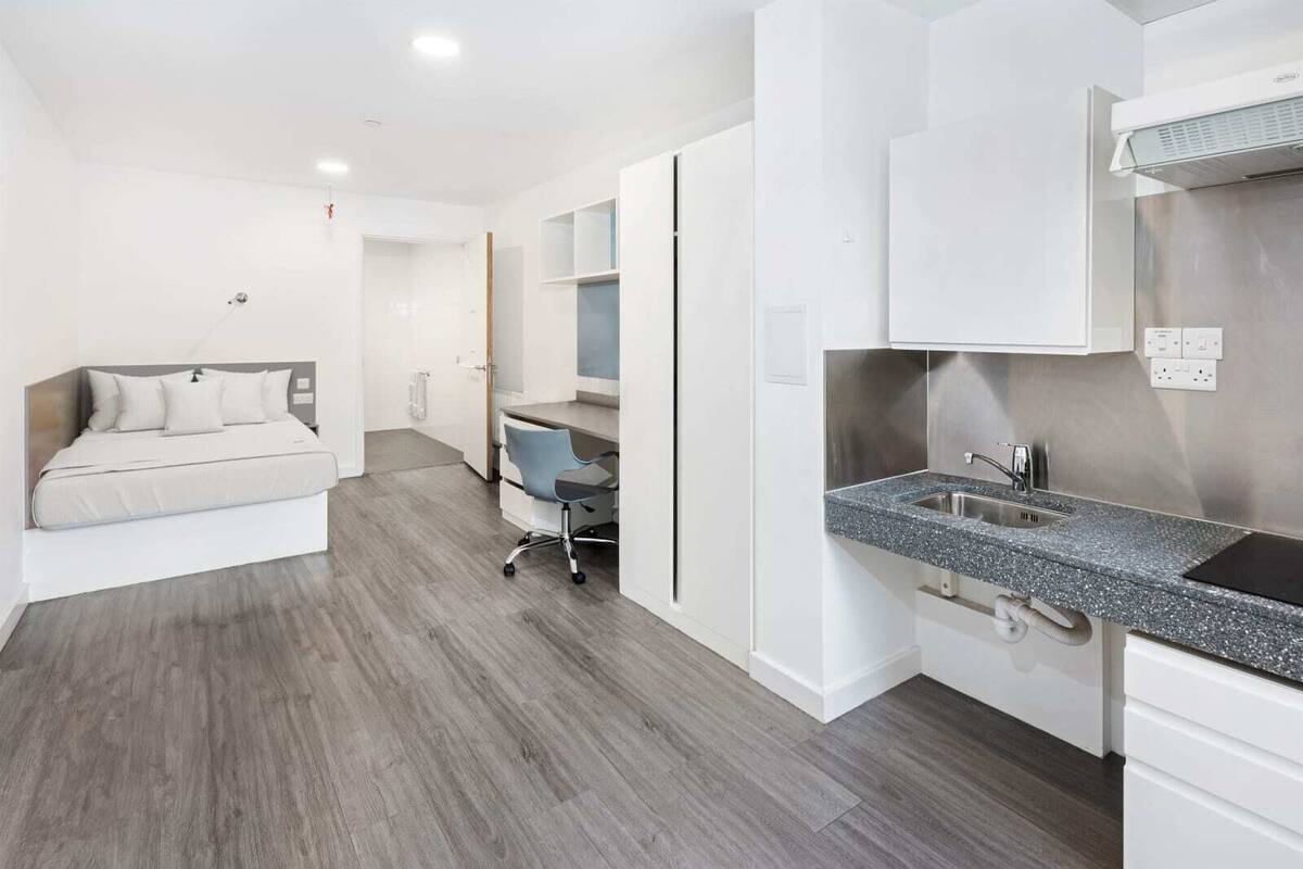 A modern, compact hotel room with a bed, a desk, and a kitchenette.
