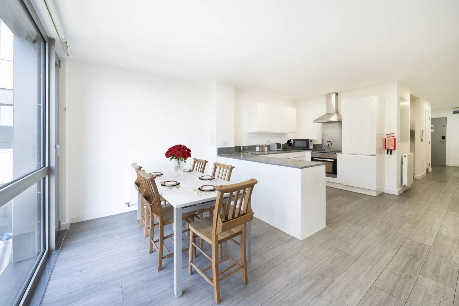 A modern kitchen with white cabinetry, a central island, and a dining area with wooden chairs.
