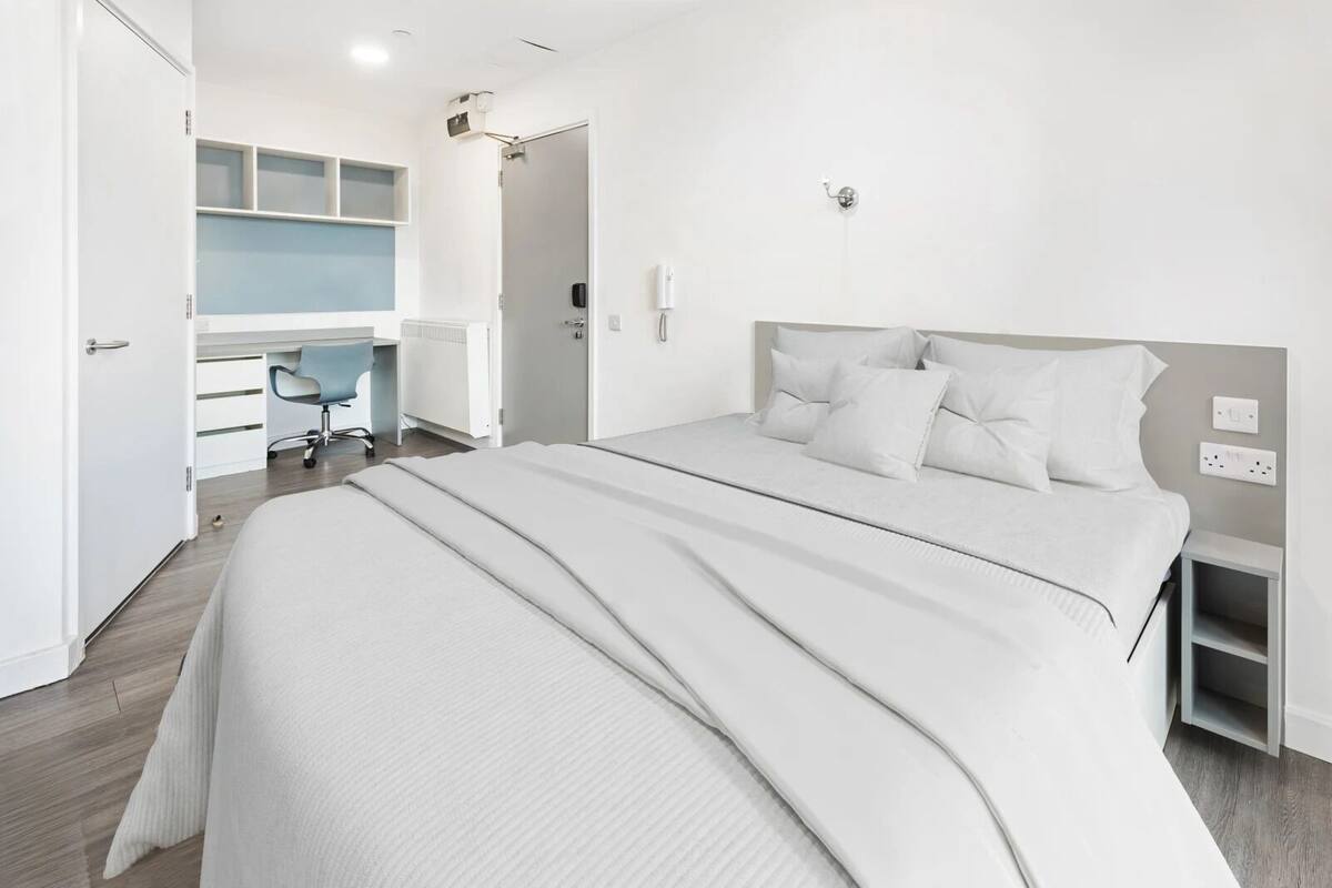 A modern hotel room with a large bed, a desk, and a chair.