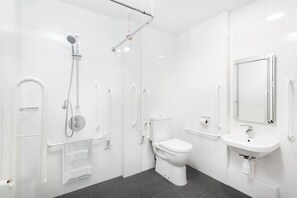 A modern bathroom with a shower, toilet, and sink, equipped with grab bars and a handrail. - Chapter Lewisham in London - Campus Accommodation (London)