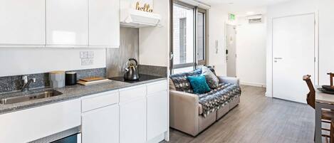 A modern kitchen with white cabinets, a stainless steel sink, and a kettle on the counter.