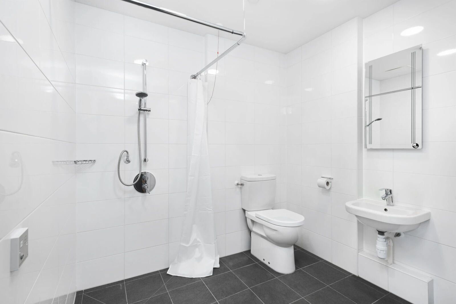 Ein modernes Badezimmer mit weißen Fliesen, einer Dusche, einer Toilette und einem Waschbecken.