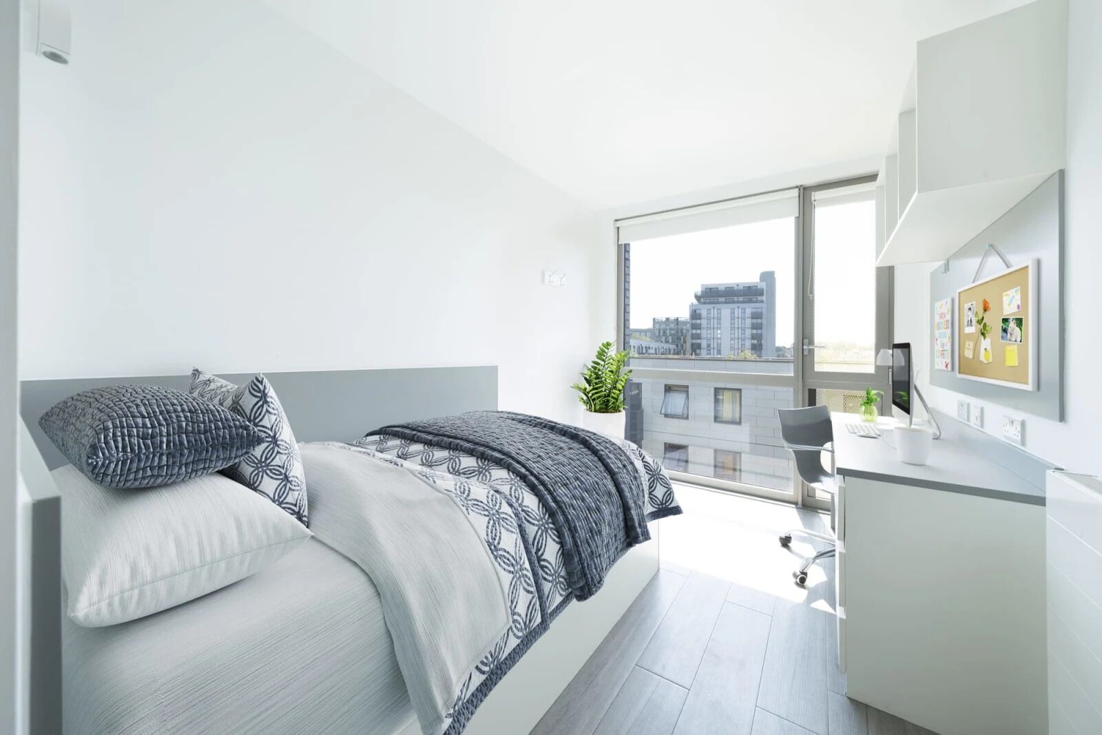 Un dormitorio moderno con cama, escritorio y ventana grande con vistas a un paisaje urbano.