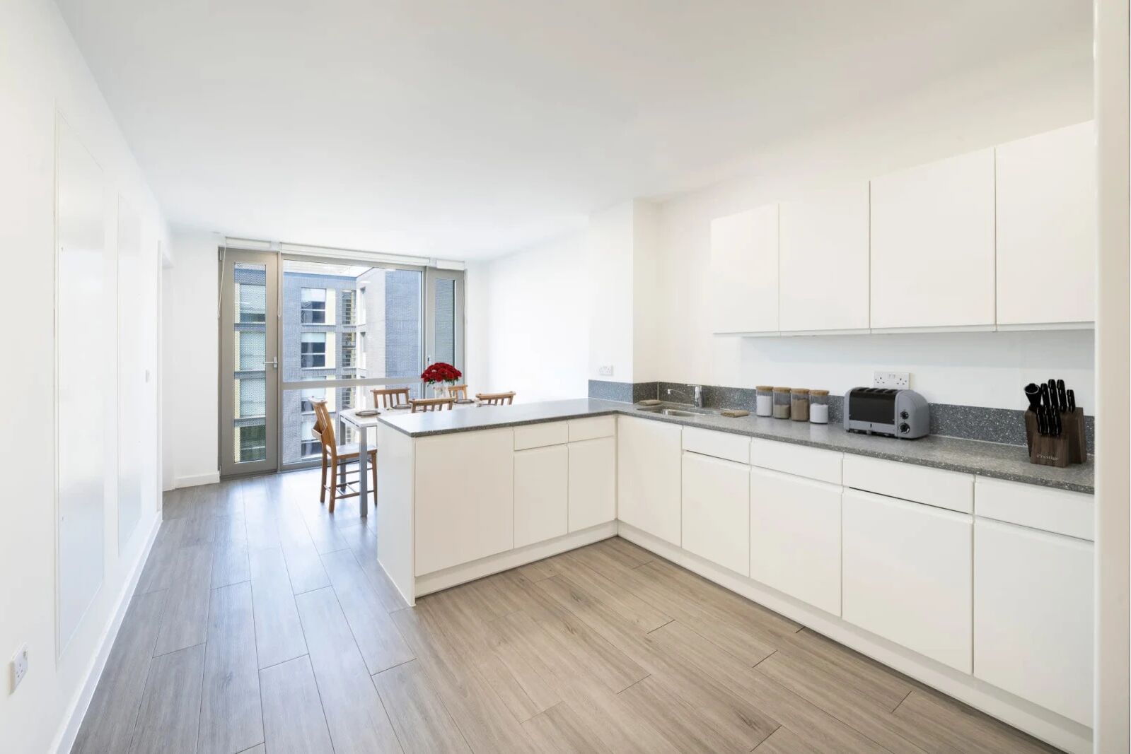 Una cocina moderna con armarios blancos, una isla central y un comedor con mesa y sillas.