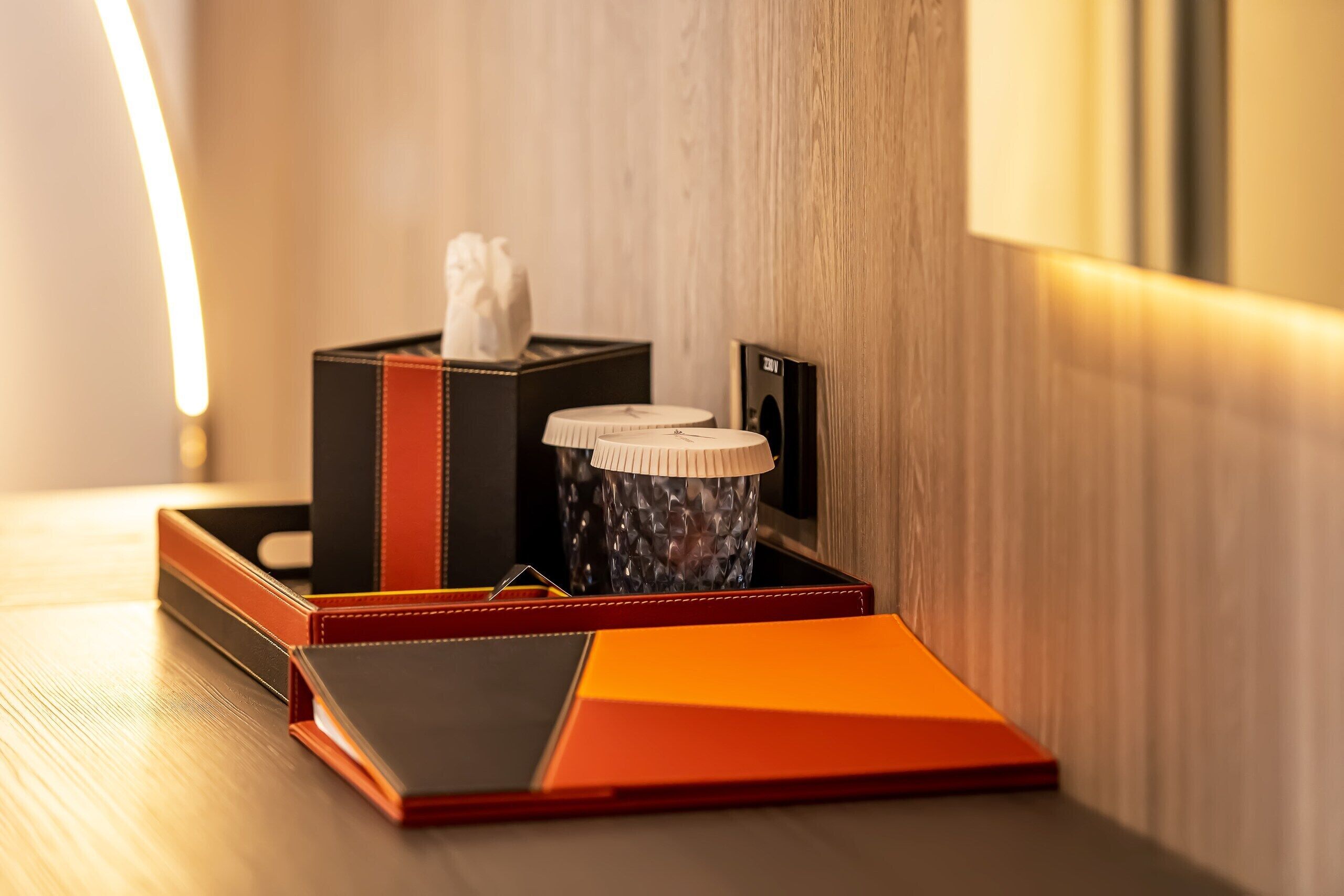 A wooden desk with a red and black box, a white tissue box, and a black and white container.