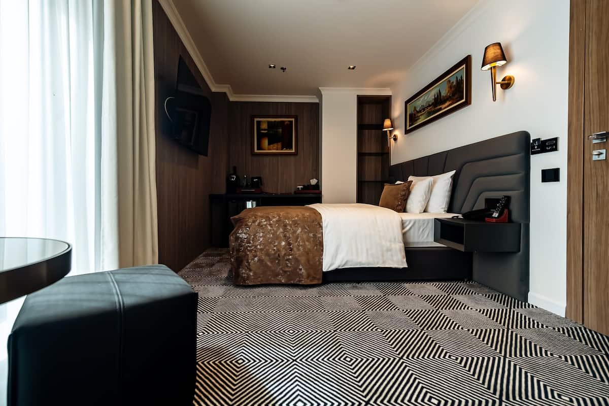 Una habitación de hotel con cama, mesita de noche, lámpara y un cuadro en la pared.