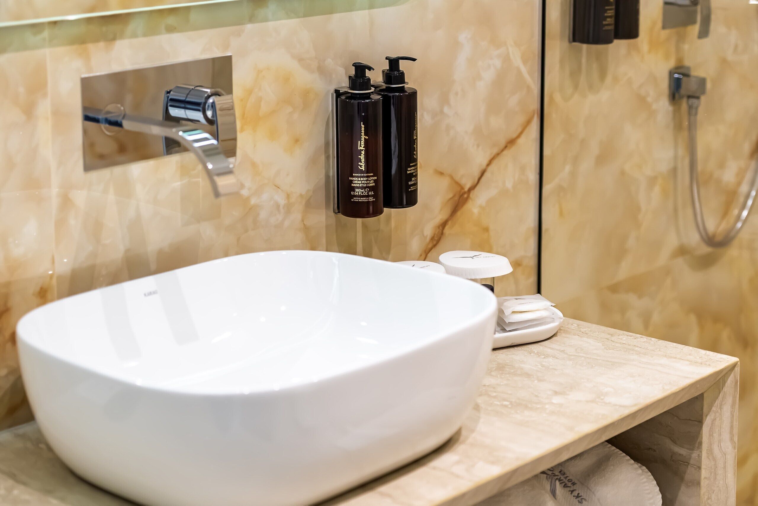 Un baño con un lavamanos blanco, dos botellas de champú negras y un cabezal de ducha.