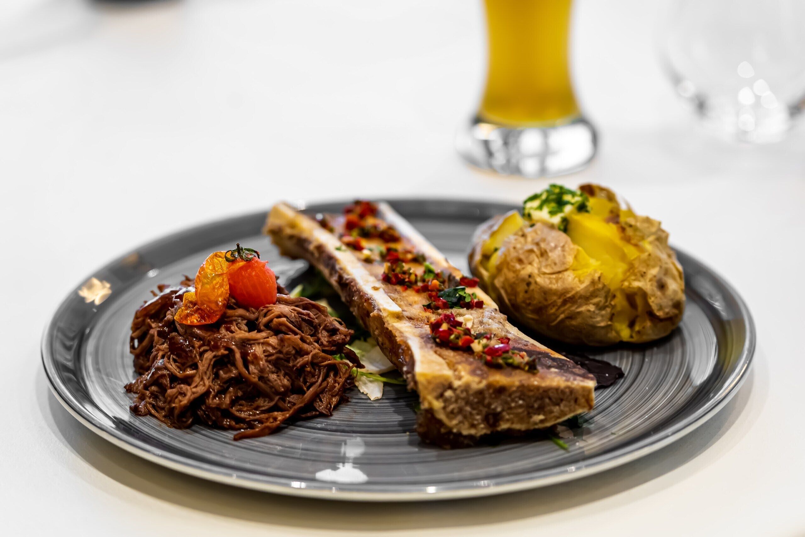 A plate with shredded meat, a roasted bone, and a baked potato.